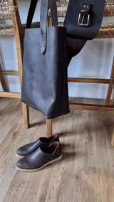 Bolso tote de cuero color marrón oscuro con doble asa larga de cuero y remaches metálicos.