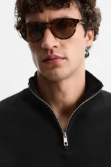 Jersey negro de punto de algodón, corte recto, cuello perkins con cremallera metálica y mangas largas terminadas en rib.