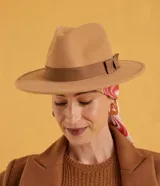 Sombrero de estilo fedora color tostado, con ala de tamaño mediano y cinta decorativa en contraste de color marrón alrededor de la copa. Confeccionado íntegramente en poliéster.