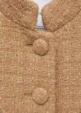Chaqueta corta color beige de tweed con cuello mao, cierre frontal con botones y cuatro bolsillos delanteros con solapa.