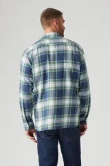 Camisa de franela a cuadros azules, verdes y blancos, de corte recto, manga larga y dos bolsillos frontales con solapa abotonada.
