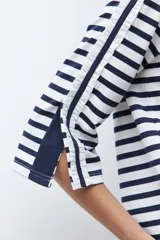 Buzo de cuello redondo con estampado de rayas horizontales blancas y azul marino. Presenta mangas de largo 3/4 con un panel lateral en contraste, botones decorativos y terminación en volados.