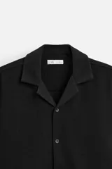 Camisa color crudo de corte regular fit, confeccionada en tejido con textura. Tiene cuello bowling, manga corta, bajo con aberturas laterales y cierre frontal con botones.