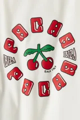 Remera blanca de algodón con cuello y mangas con ribete rojo. Estampado con cerezas y texto "Ibiza" en rojo.
