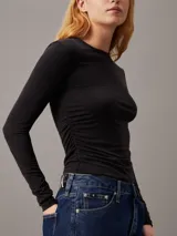 Remera negra de punto modal elástico, con cuello redondo, mangas largas y detalle plisado en un lateral.