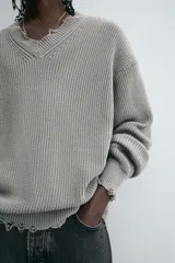 Sweater gris de punto con cuello en V, manga larga y terminaciones irregulares con efecto desgastado.