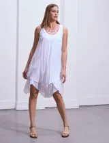 Vestido blanco de gasa con escote redondo bordado con apliques metálicos. Tiene forro interno a tono y ruedo en capas asimétricas.