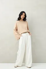 Sweater color beige de tejido de punto, con cuello redondo y mangas largas acampanadas con botones decorativos en los laterales.