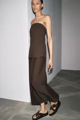 Vestido midi marrón confeccionado en hilatura 24% de lino. Escote recto y hombros descubiertos. Cierre en espalda con cremallera oculta en costura.