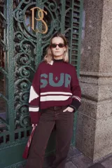 Sweater de punto grueso color borgoña con cuello alto, mangas largas y diseño con la palabra "SUR" en letras grandes color verde y una franja horizontal blanca.