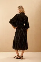 Vestido largo negro con estampado de lunares dorados, mangas al codo y corte amplio con ajuste elástico en la cintura. Presenta bordados de lentejuelas y mostacillas en el escote y mangas.