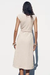 Vestido midi color crudo con jacquard floral, escote pico cruzado, manga sisa caída y cinturón ajustable con hebilla.