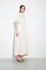 Vestido camisero largo de manga larga, color blanco con finas rayas verticales en tono claro, con cuello solapa y abotonadura frontal. Posee un calce amplio y bolsillos laterales.