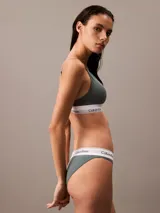 Conjunto de ropa interior Calvin Klein, modelo Modern Cotton, color gris, compuesto por un corpiño triangular con breteles finos regulables y una bombacha tipo tanga. Ambos con banda elástica blanca con logo de la marca.