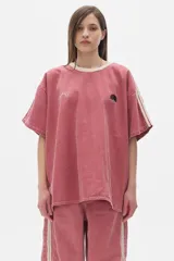 Remera de denim color rosa con efecto lavado, corte oversized, cuello redondo en contraste color crema, mangas cortas con rayas laterales y bordados en el frente.