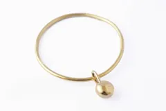 Pulsera dorada tipo brazalete con dije colgante en forma de esfera.