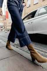 Botín de serraje color marrón, con tacón ancho en bloque y punta redonda. Presenta un detalle de pespunte en el cuerpo y cierre mediante cremallera lateral.