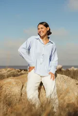 Camisa celeste a rayas verticales blancas, de corte holgado, con cuello clásico y botones dorados.