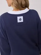 Sweater color ladrillo con cuello redondo en color crema. Estampado frontal con el texto 'Malibu Rusty' y un logo con forma de flor. Corte holgado.
