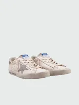 Championes Golden Goose modelo Super Star, color blanco con detalles en gris y suela color crema. Presentan efecto desgastado y estrella distintiva de la marca en el lateral.