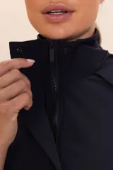 Campera negra de corte ancho y mangas raglán, confeccionada en tejido ligero y transpirable resistente al agua. Cuenta con capucha alta con cierre de cremallera y botones, mangas y barra ajustables, y bolsillo funcional en la parte delantera.