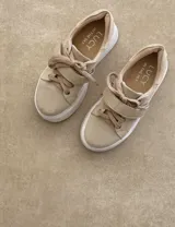 Zapatillas deportivas urbanas con capellada negra, detalles en beige y suela blanca.