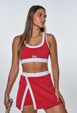 Conjunto deportivo rojo con detalles en blanco, compuesto por un top con logo 'bk.' y una falda-short con abertura lateral.