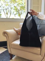 Bolso tipo tote bag negro de cuero, con costuras a la vista y manijas cortas.