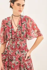 Vestido corto con estampado floral en tonos rojo y gris, escote en V, mangas cortas con volados, frunces en delantero y espalda, y bolsillos delanteros.