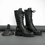 Borcego de cuero vacuno color negro, con suela de goma artesanal, caña alta con aplique capitoneado desmontable y horma de punta redonda.