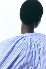 Blusa de popelina de algodón a rayas celestes y blancas, con cuello mao, abertura en V y botones frontales. Mangas globo tres cuartos de corte raglán con puños finos y bajo recto.