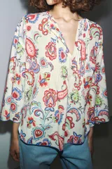 Camisa de algodón color crudo con estampado de cachemir en tonos rojo, azul y verde. Tiene cuello redondo, escote en pico, manga tres cuartos acampanada y bajo asimétrico redondeado.
