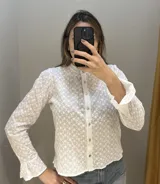 Camisa blanca de broderie de algodón con cuello mao, mangas largas con volados y botones de nácar.