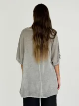 Blusa gris de lino y algodón, de corte amplio, con cuello redondo y mangas cortas con terminación desflecada. Presenta un volante diagonal en el frente.