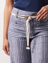 Pantalón de lino a rayas verticales azules y blancas, con corte ancho, pretina con pasadores, cierre y botones. Incluye cinto de soga con nudo.