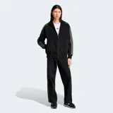 Pantalón de jean negro de corte ancho con tres tiras plateadas a los costados y logo de Adidas bordado en el muslo.