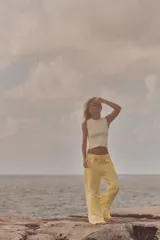 Pantalón de mujer color amarillo pálido, de corte ancho y tejido fluido. Tiene tiro medio, cintura elástica ajustable con cordones, bolsillos laterales y falsos bolsillos de vivo en la espalda.