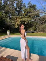 Conjunto de bikini blanco tejido a crochet, compuesto por un top triangular con volados y una pollera larga calada con cordón ajustable en la cintura.