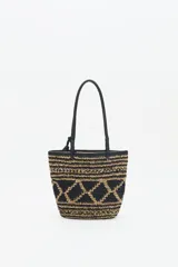 Bolso tote tejido en raffia color negro y beige, con vivos y correas en cuero sintético negro. Tiene cierre interno con snap metálico y forro de algodón.