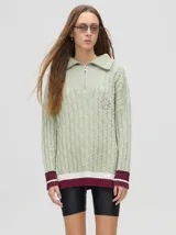 Sweater tejido en ochos color verde claro, con cuello polo con cierre de cremallera, puños a rayas en color borgoña y blanco, y logo bordado en el pecho. Corte por debajo de la cadera.