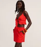 Short pollera de color rojo confeccionado en tejido de viscolino, una mezcla de lino y viscosa. Presenta un diseño de cintura fija con cierre de cremallera lateral y bolsillos frontales con solapa.