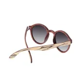 Lentes de sol Indie modelo Hill con montura redonda de madera color marrón y beige, y lentes grises degradadas.