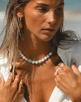 Collar corto de cuentas redondas de cerámica blanca con estampado floral en tonos azules y verdes, engarzadas con pequeñas cuentas turquesas. Cierre de acero.