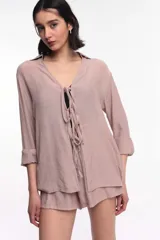Camisa beige de manga larga con cuello y lazo de ajuste en el escote.