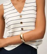 Chaleco sin mangas de punto, color blanco con rayas horizontales finas en negro. Presenta escote en V y cierre frontal con botones marrones.