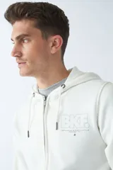 Campera de felpa color beige con cierre frontal, capucha con cordón ajustable, bolsillos laterales y logo estampado en el pecho.