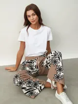 Pantalón de tela color marrón con estampado de flores blancas y negras, de corte palazzo con bolsillos laterales y cintura con cordón.