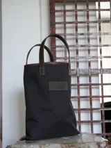 Bolso matero de lona color azul con detalles en cuero marrón, con asas cortas y logo de la marca en cuero.