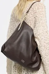 Bolso de mano tipo shopper de cuero color marrón oscuro, con estructura blanda y asa extraíble. Incluye logo metálico de la marca Bimba y Lola, acabados metálicos, bolsillo interior e interior con etiqueta de tejido.