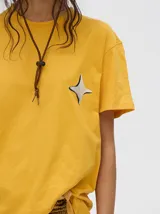 Remera amarilla de corte cuadrado y holgado, con estampado de estrella plateada con borde negro en el frente.